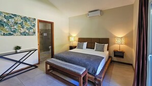A bedroom with a bed, bedside lamps, a bench, a wall-mounted air conditioner, and a door leading to a bathroom. - SOSUA Luxury 9-BDR Villa : 20 Guests : POOL (Sosúa)