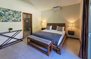 A bedroom with a bed, bedside lamps, a bench, a wall-mounted air conditioner, and a door leading to a bathroom. - SOSUA Luxury 9-BDR Villa : 20 Guests : POOL (Sosúa)