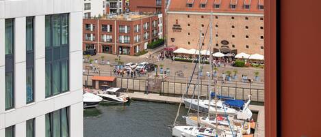 A marina with boats docked, a building with a red roof, and a view of a cityscape in the background.