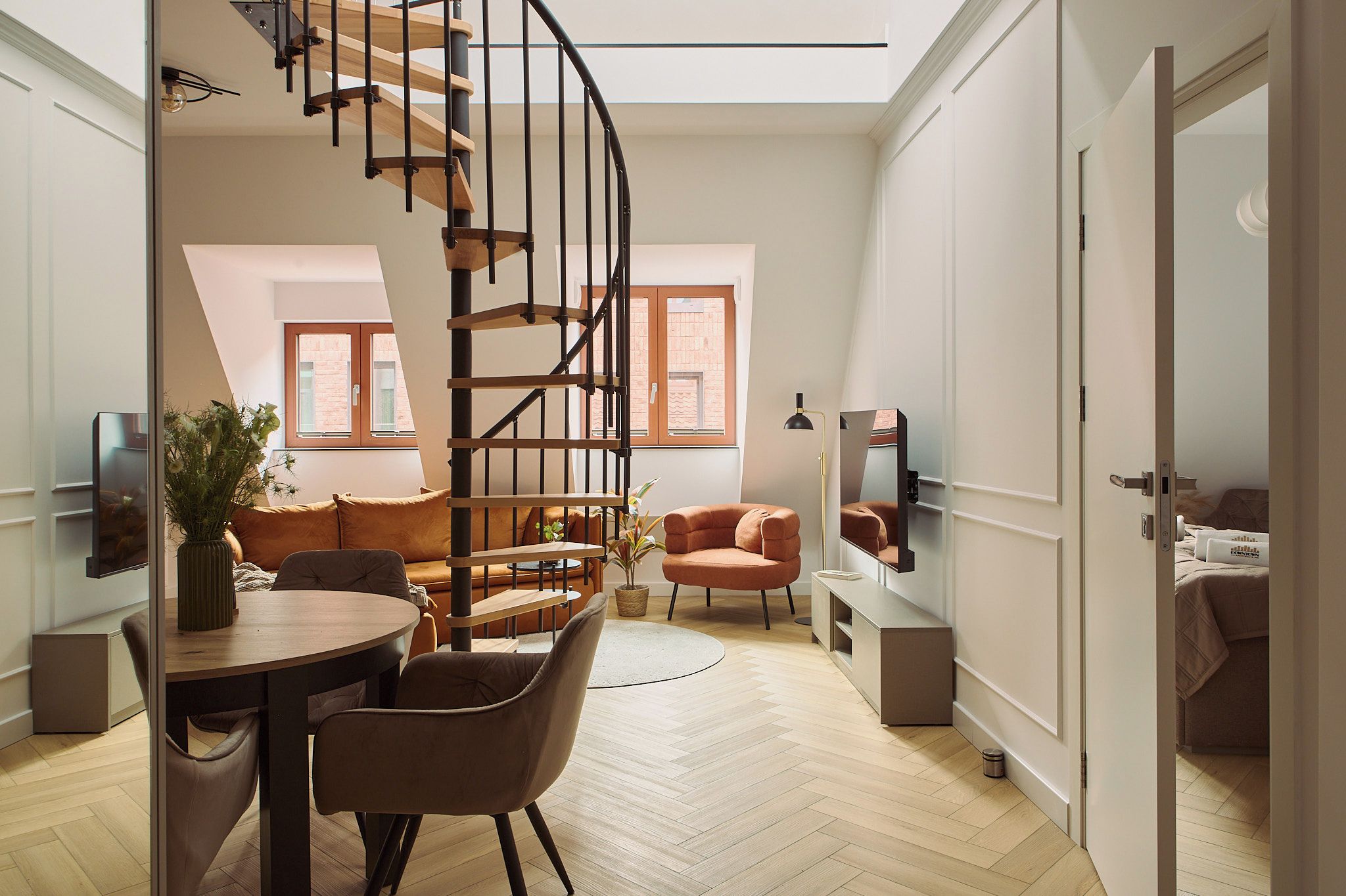 Ein modernes Interieur mit einer Wendeltreppe, einem Essbereich, einer Couch und einem Fernseher.