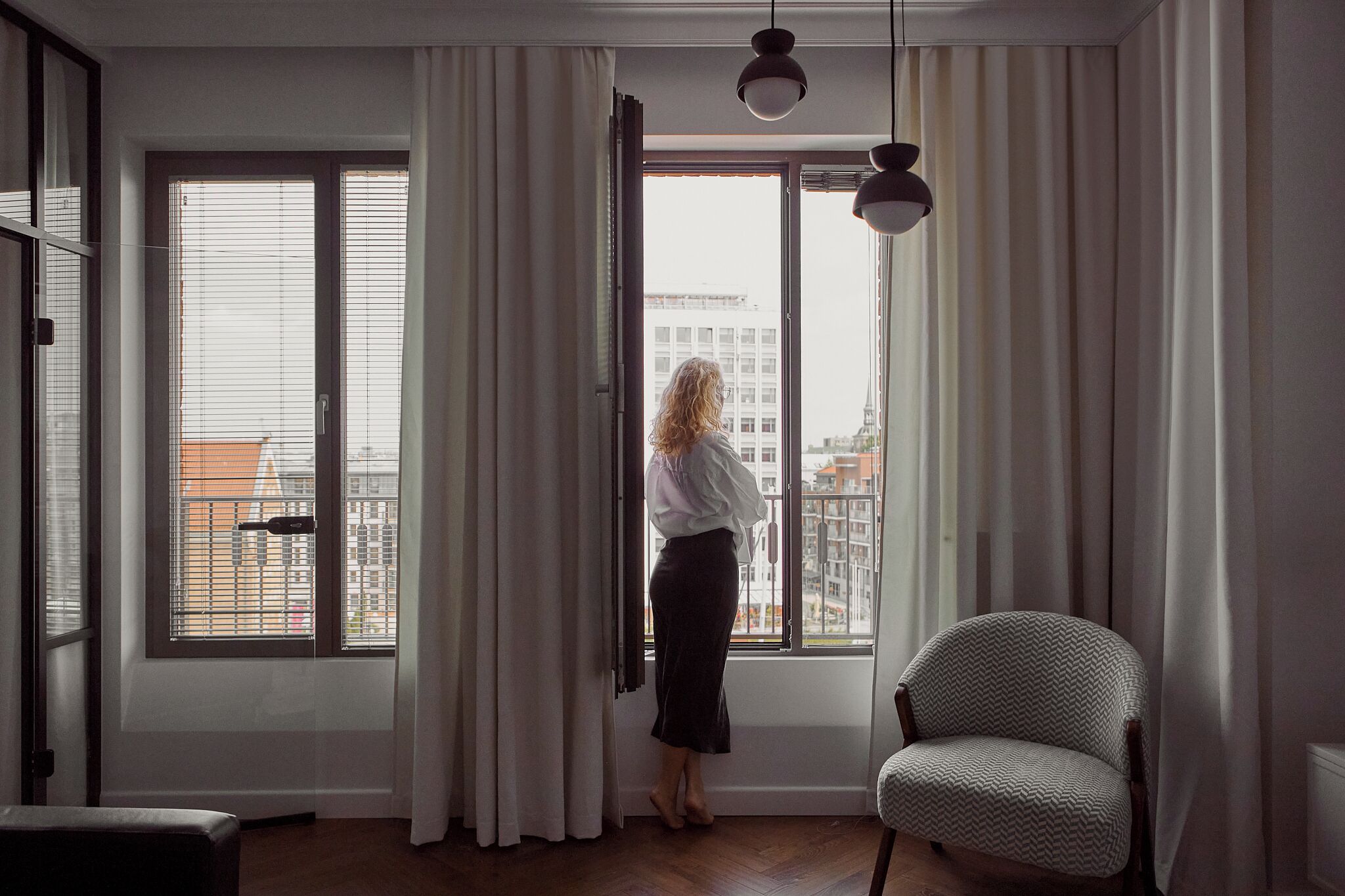 A room with large windows, a chair, and a person standing by the window.