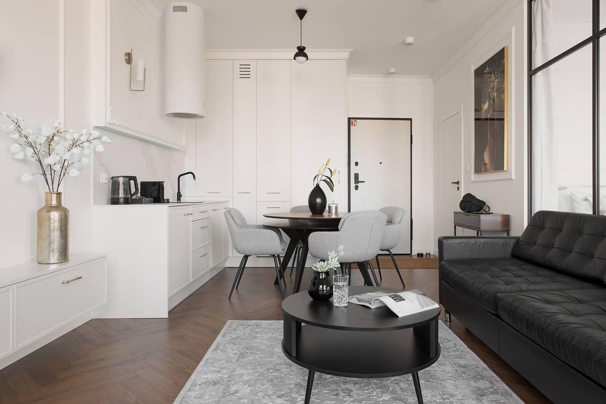 Un salon moderne avec un canapé noir, une table basse ronde et un coin repas comprenant une table et des chaises.