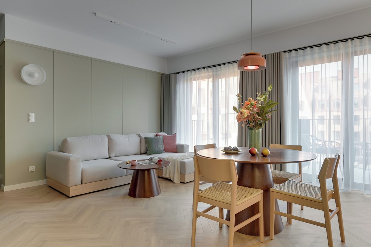 A modern living room with a sofa, a round wooden table, and a dining area with chairs.