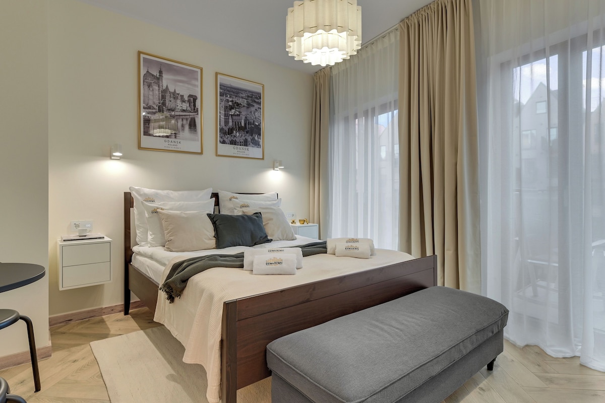 A hotel room with a bed, bedside tables, a bench, and two framed pictures on the wall.