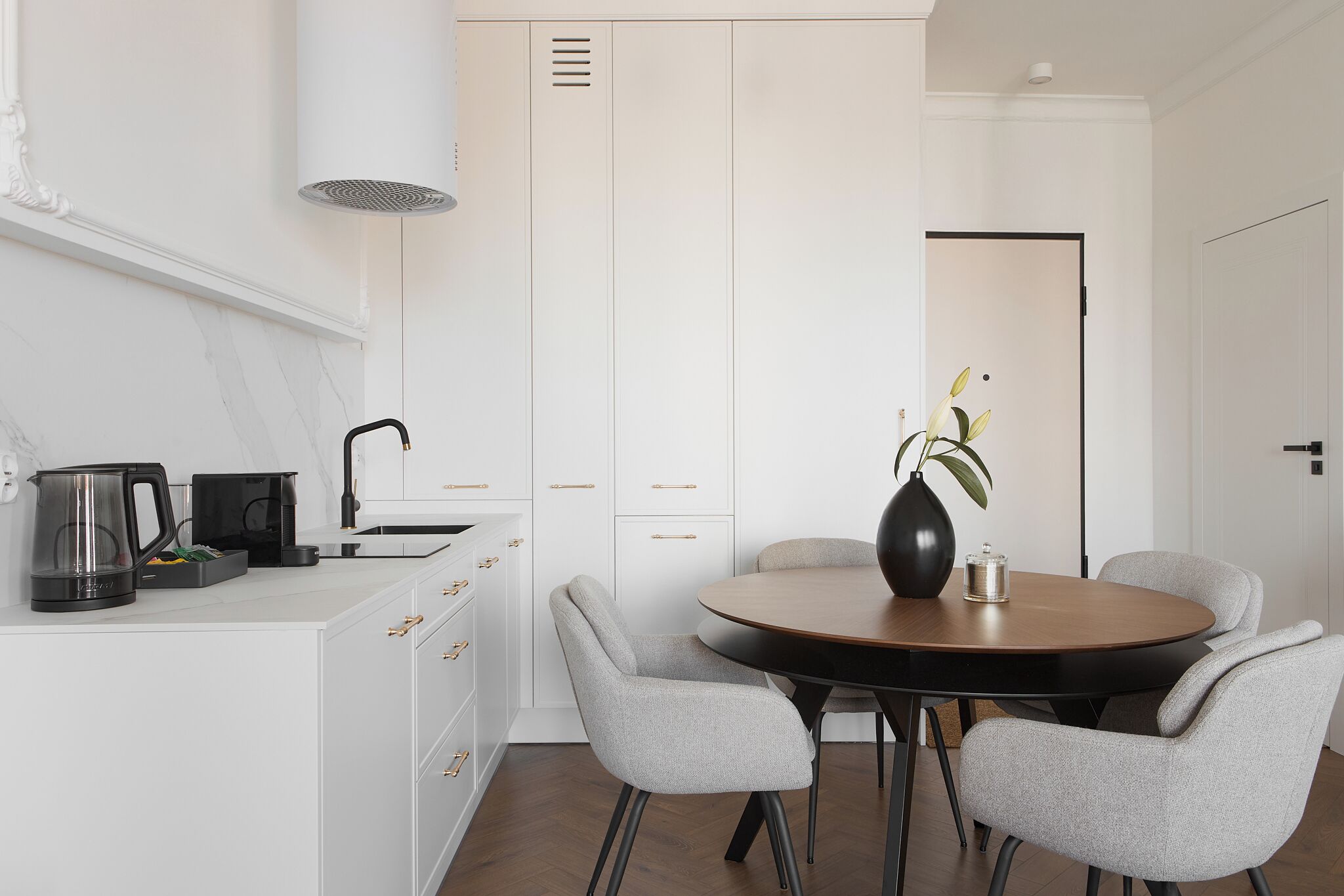 Une cuisine moderne avec des meubles blancs, une table de salle à manger ronde et deux chaises grises.