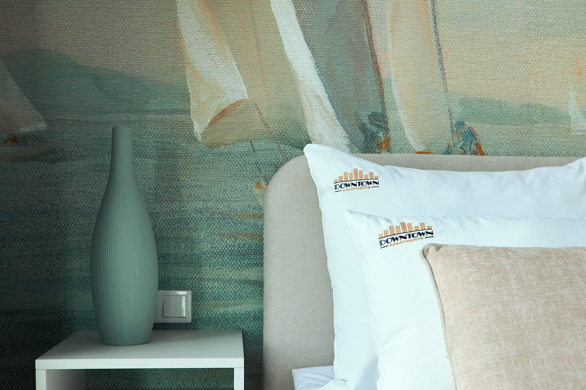 A bedroom with a bed, a nightstand, a vase, and a wall with a cityscape design.