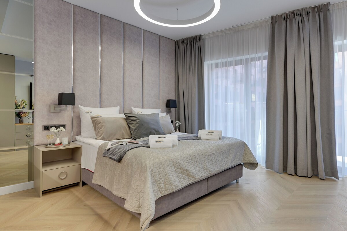 A modern bedroom with a large bed, bedside tables, a mirror, and a view of the outdoors.