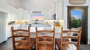 A spacious kitchen with white cabinets, a wooden dining table, and a view of the outdoors through a door.