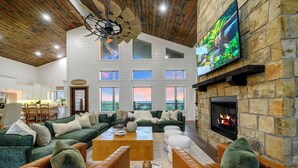 A spacious living room with a fireplace, comfortable seating, and a large TV mounted on the wall.