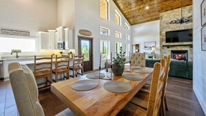 A spacious kitchen with a long wooden table, multiple chairs, and a stone fireplace.