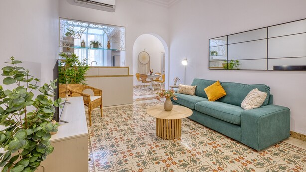 A living room with a green sofa, a round coffee table, and a dining area with wicker chairs. - Charming and cosy maisonette in Sliema RABE1-1 (Sliema)