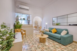 A living room with a green sofa, a round coffee table, and a dining area with wicker chairs. - Charming and cosy maisonette in Sliema RABE1-1 (Sliema)