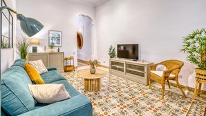 A living room with a teal sofa, a round coffee table, a wicker chair, and a TV on a cabinet. - Charming and cosy maisonette in Sliema RABE1-1 (Sliema)