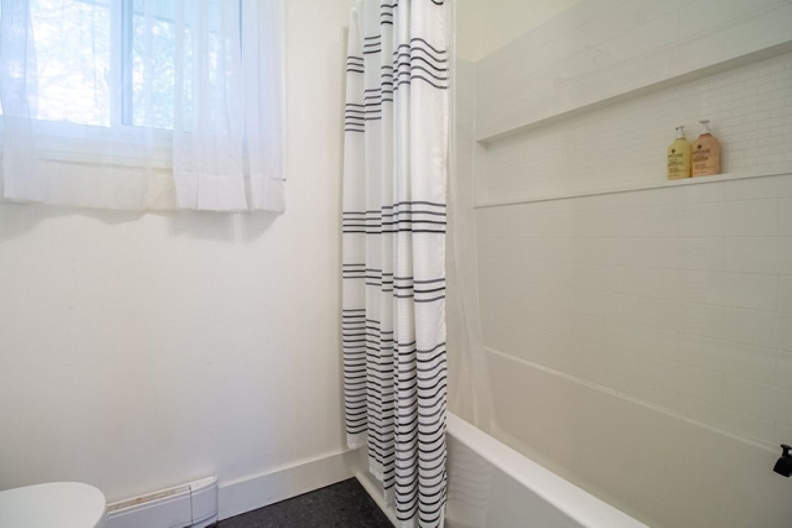 Une salle de bain avec une baignoire blanche, un rideau de douche à rayures noires et une fenêtre avec des rideaux légers.