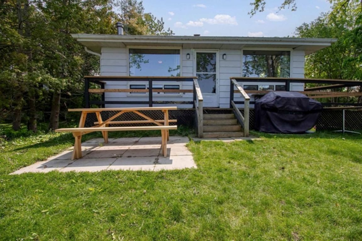 A small, single-story house with a front porch, a wooden bench, and a barbecue grill.