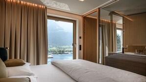 Una habitación de hotel moderna con una cama grande, vistas a una montaña y un lago, y muebles de madera.