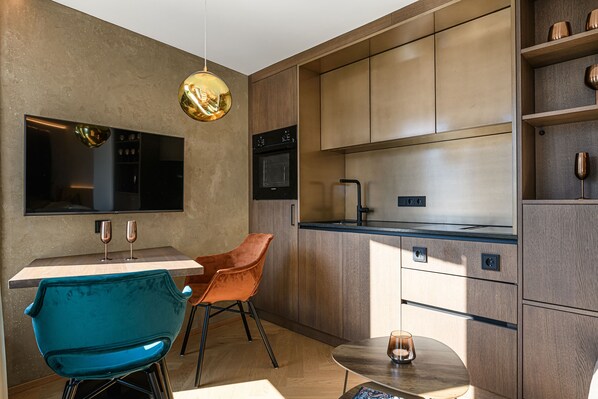 Una cocina moderna con una televisión de pantalla plana, horno integrado y un comedor con una silla azul y una pequeña mesa.