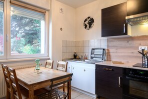 A modern kitchen with a dining table, chairs, a window with blinds, a clock, and a built-in oven.