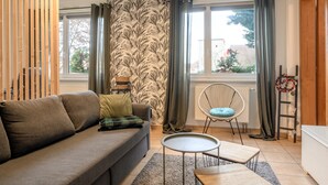 Een woonkamer met een bank, een rond bijzettafeltje, een stoel, een radiator en een raam met gordijnen.