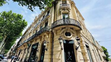 A historic building with ornate architecture, including a balcony with intricate ironwork, large windows, and a prominent entrance with a decorative door.