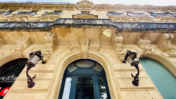 Fachada de edificio ornamentada con un arco central y dos faroles simétricos.