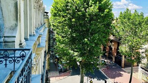 Una calle arbolada con arquitectura clásica, una acera y un cielo azul despejado.