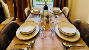 Mesa de comedor preparada para cuatro personas, con platos, cubiertos y copas de vino, ubicada frente a una ventana con vistas a árboles.