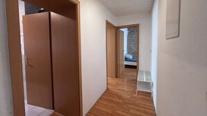 A hallway with wooden flooring, a wardrobe, and a bed with a stone wall in the background. - AriProp Zeitz Stone Wall Apartment - 8 guests. (Zeitz)