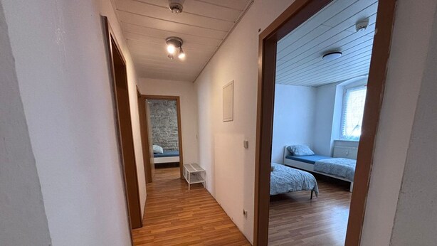 A narrow hallway with wooden flooring leading to a bedroom with a bed and a window. - AriProp Zeitz Stone Wall Apartment - 8 guests. (Zeitz)