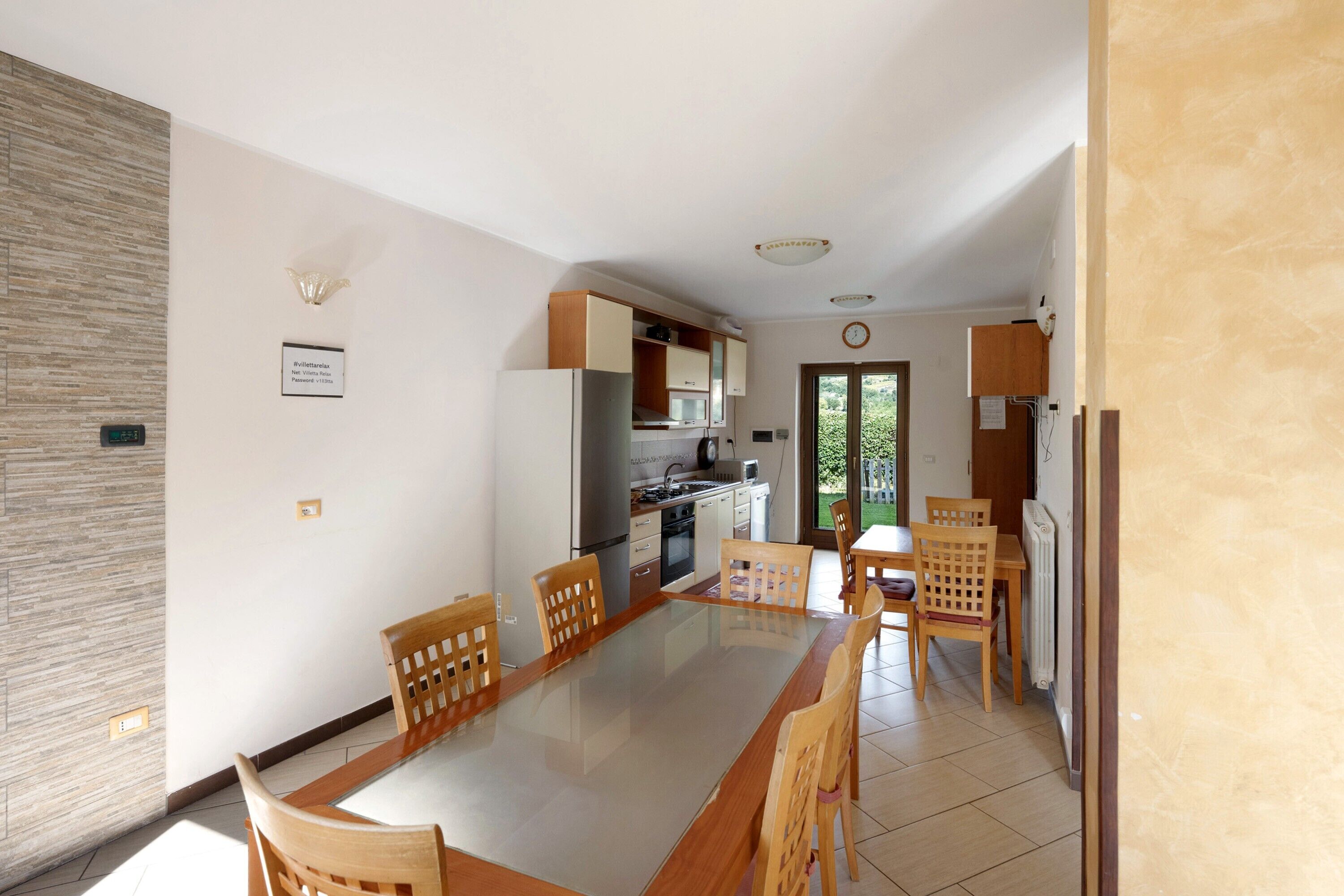 A modern kitchen with built-in appliances, a dining area with a glass table, and wooden chairs.