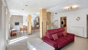 A spacious living area with a red sofa, a white ottoman, and a dining table with chairs. There is a staircase with wooden railings and a modern light fixture. - Villa 'Relax' with Mountain View, Wi-Fi and Air Conditioning (Ruviano)