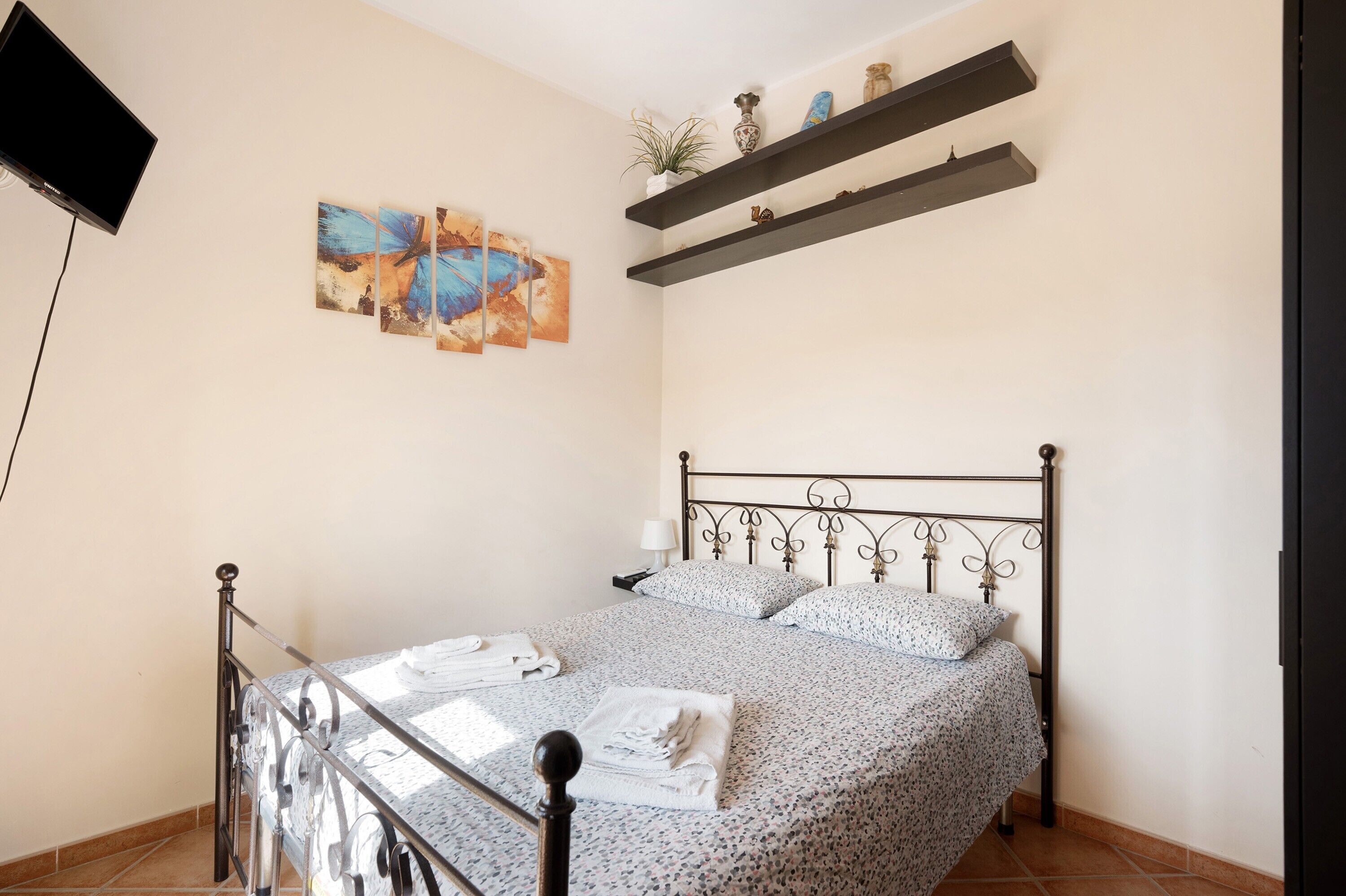 A bedroom with a bed, a TV, artwork, and shelves.