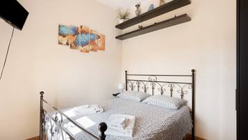 A bedroom with a bed, a TV, artwork, and shelves.