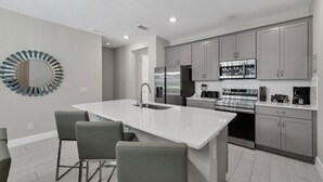 A modern kitchen with a central island, grey cabinetry, stainless steel appliances, and a unique circular wall decoration.