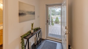A modern entryway with a glass door leading to a deck, a console table with greenery, and a painting on the wall. - Cozy 4 bedroom house for rent in the heart of the Mountains.  Minutes to Cannon. (Franconia)