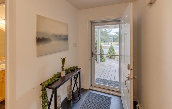 En moderne entré med en glasdør, der fører til en terrasse, et konsolbord med grønne planter, og et billede på væggen.