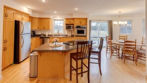 A modern kitchen with wooden cabinets, stainless steel appliances, a central island, and a dining area with wooden chairs. - Cozy 4 bedroom house for rent in the heart of the Mountains.  Minutes to Cannon. (Franconia)