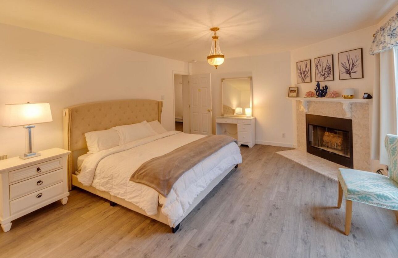 Un dormitorio con una cama grande, mesitas de noche, un espejo, una chimenea y un banco.