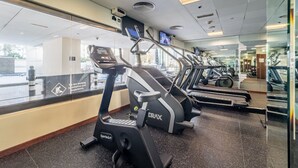 Une salle de sport équipée de tapis de course, de vélos d’exercice et d’un mur recouvert de miroirs.