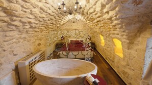 Ein Zimmer mit Steinwänden, einem Bett, einem runden Tisch und einer Chandelüster.