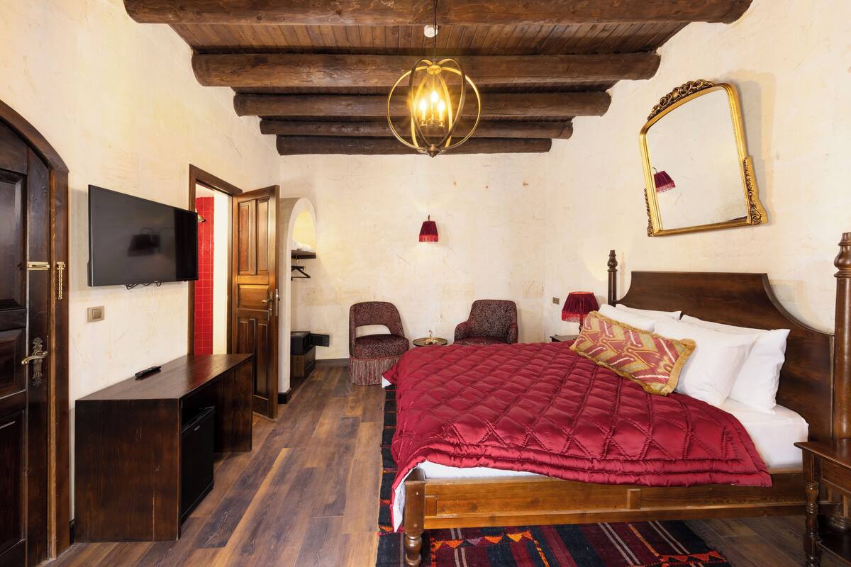 Een slaapkamer met een houten bed, een televisie, een spiegel en een kroonluchter.