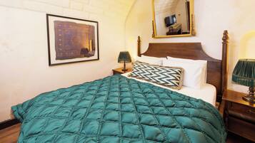 Una cama bien hecha con colcha color turquesa, cabecera de madera, una obra enmarcada en la pared y un espejo sobre la cama.