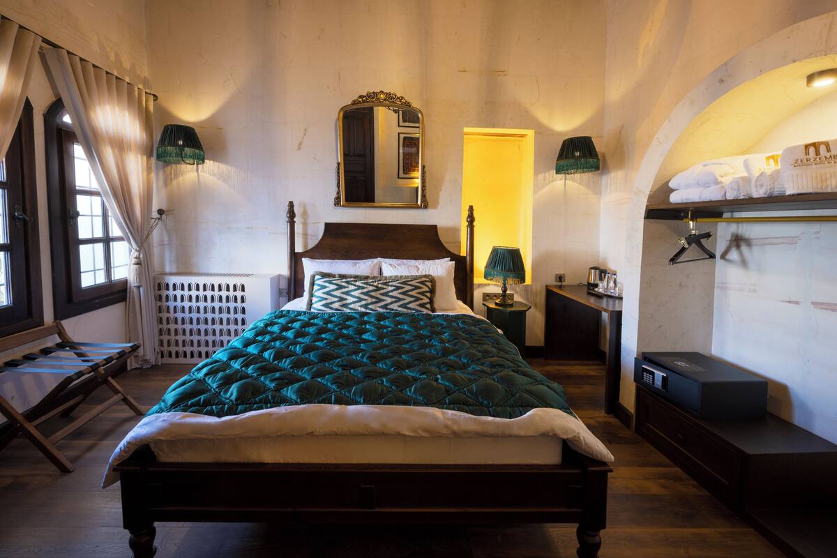 Een slaapkamer met een groot bed, een spiegel, een dressoir, een lamp en een plank met handdoeken.