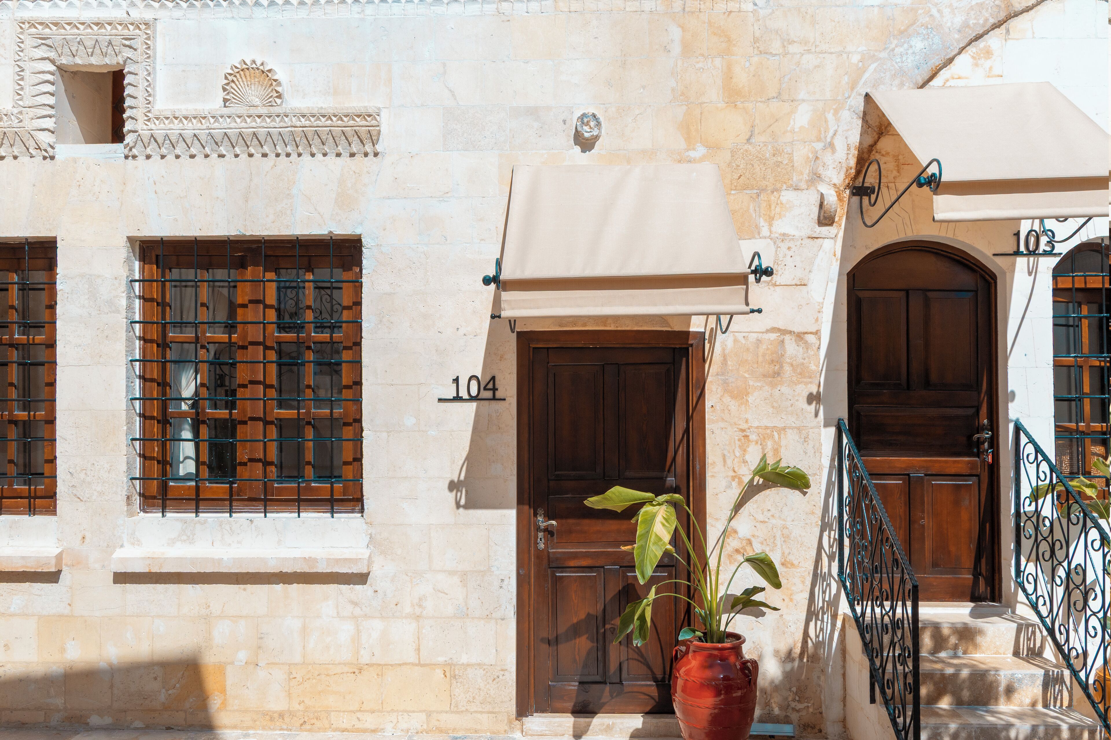 A stone building with a wooden door marked "104", a potted plant, and a metal railing.
