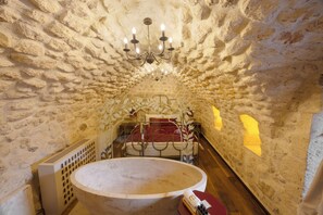 Een kamer met stenen muren, een bed, een ronde tafel en een kroonluchter.