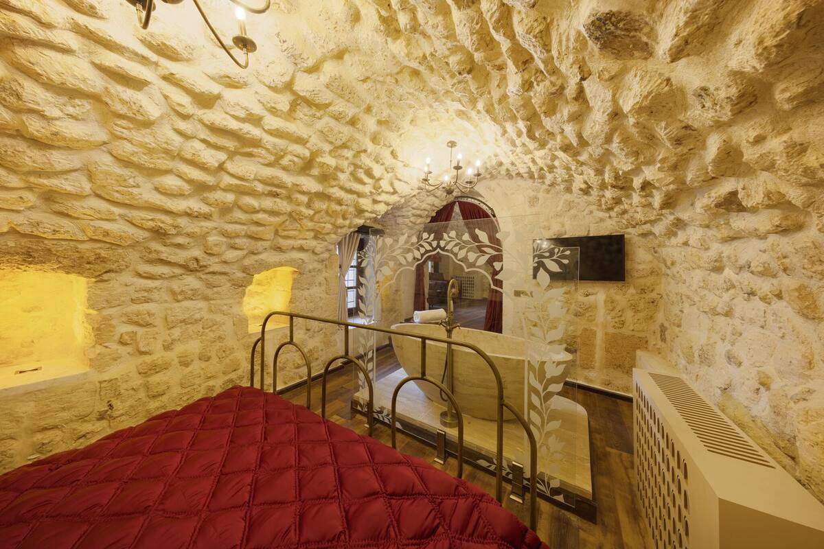 Een kamer met een stenen muur, een bed met een rode deken, een spiegel en een radiator.