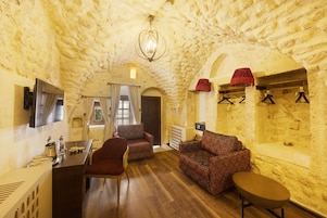 Una habitación con paredes de piedra, suelo de madera, un sofá, una silla, una mesita y una lámpara colgante.