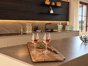 A modern kitchen with a wooden island, two wine glasses, and a knife on a cutting board.