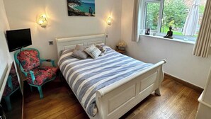 A bedroom with a bed, a chair, a TV, a window with curtains, and a painting on the wall. - 4 Bedroom House, Sleeps 8- Hot Tub, Pets, Parking (Altrincham)