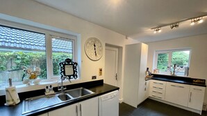 A modern kitchen with white cabinets, a black countertop, a built-in dishwasher, and a window with a view of greenery. - 4 Bedroom House, Sleeps 8- Hot Tub, Pets, Parking (Altrincham)